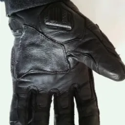 Czarna, skórzana rękawica robocza z dodatkowym wzmocnieniem na wierzchu dłoni i regulowanym mankietem, widoczna z bliska na białym tle.