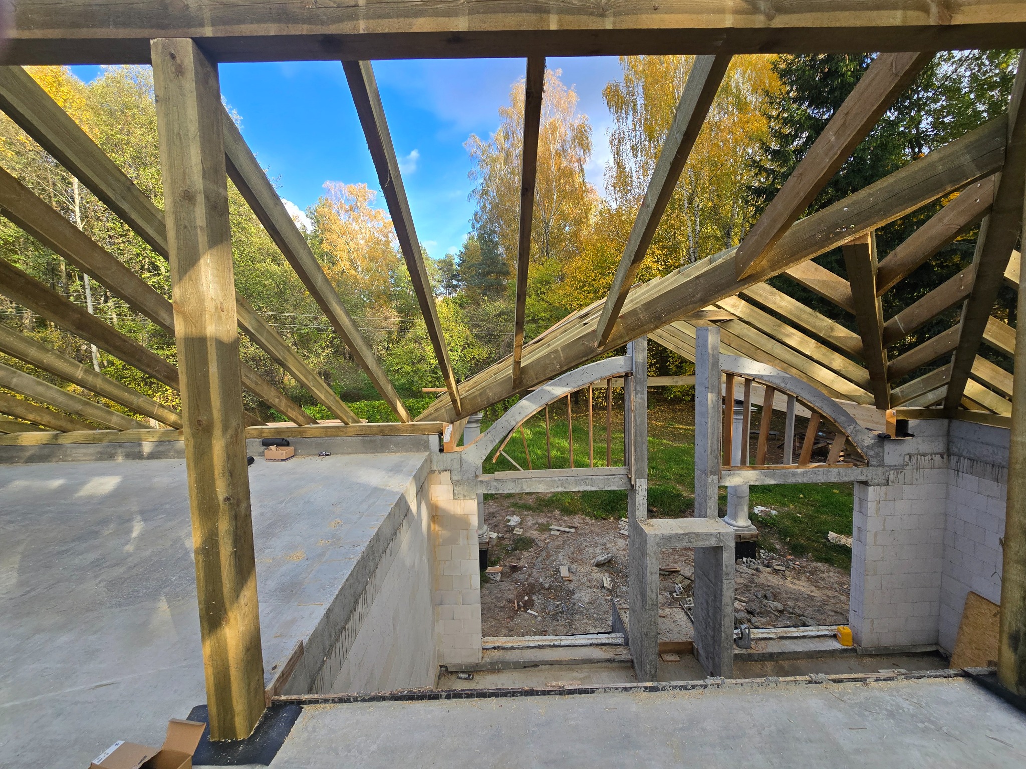 Wnętrze domu w trakcie budowy z widoczną drewnianą konstrukcją dachu na tle jesiennego krajobrazu