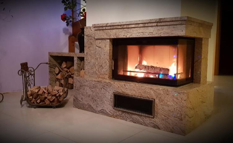 Obudowa kominkowa z jasnego kamienia z paleniskiem i dekoracyjnym koszem z drewnem obok.