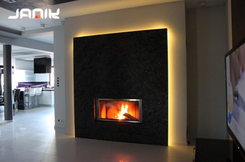 Nowoczesny kominek z czarnego kamienia z podświetleniem LED, płomień widoczny przez szklaną szybę, w tle jasne wnętrze domu.