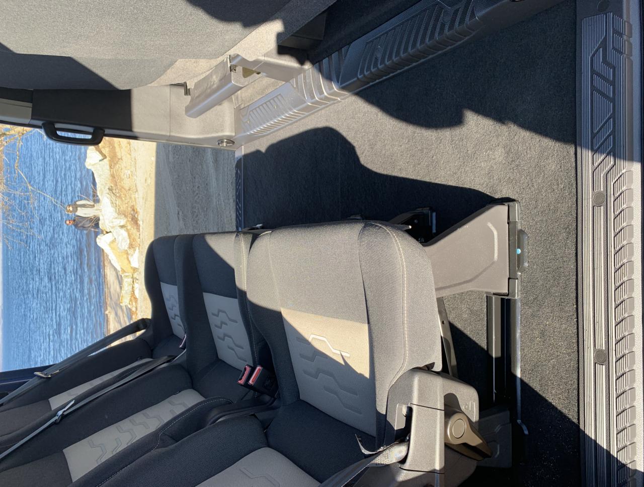 Wnętrze samochodu z widocznymi tylnymi siedzeniami, zamontowanymi relingami podsufitowymi i widokiem na brzeg jeziora z dwoma osobami na zewnątrz.