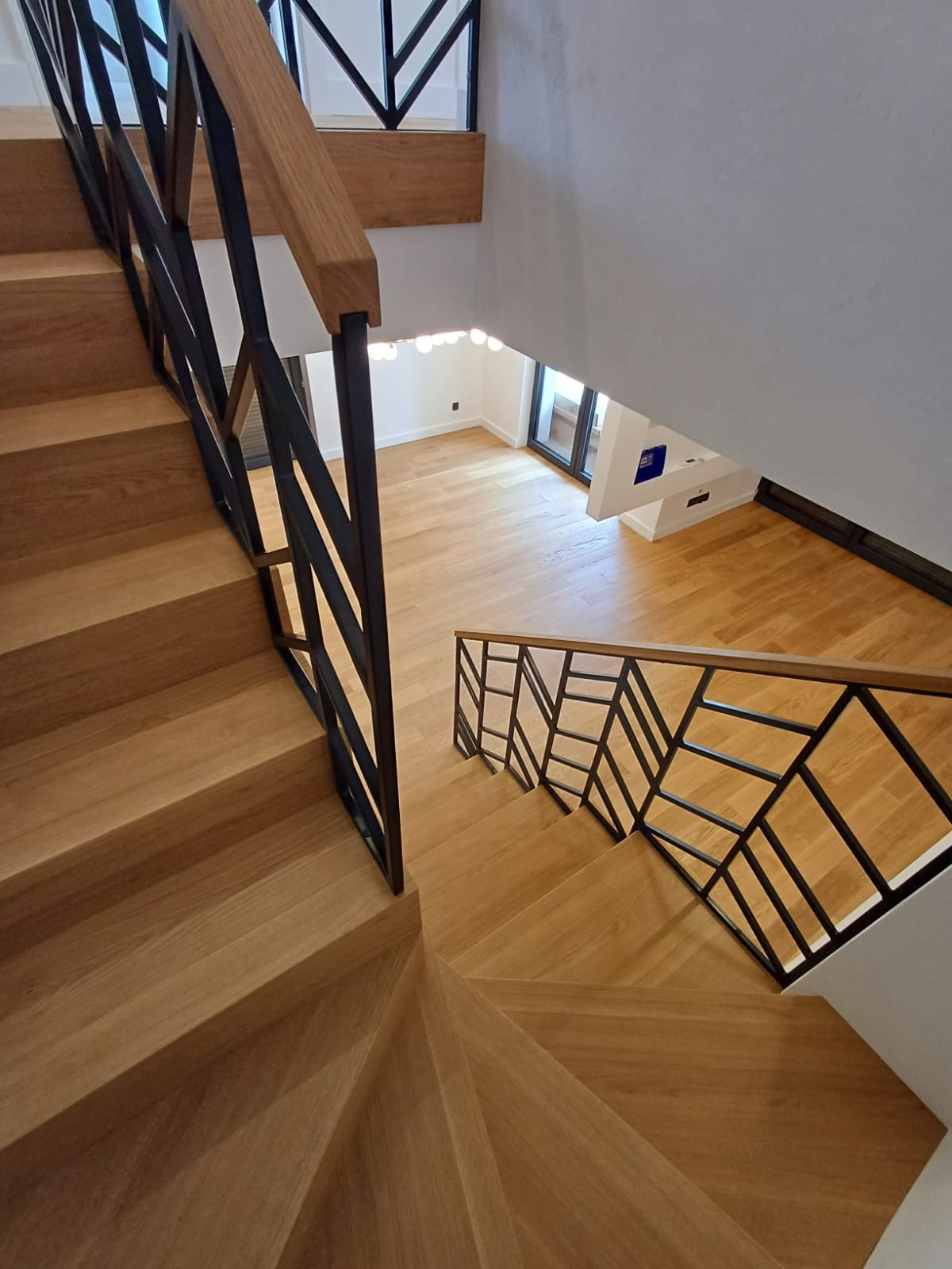 Kątowe ujęcie drewnianych schodów z czarną, geometryczną balustradą, widok z góry na jasne, drewniane podłogi w nowoczesnym wnętrzu.