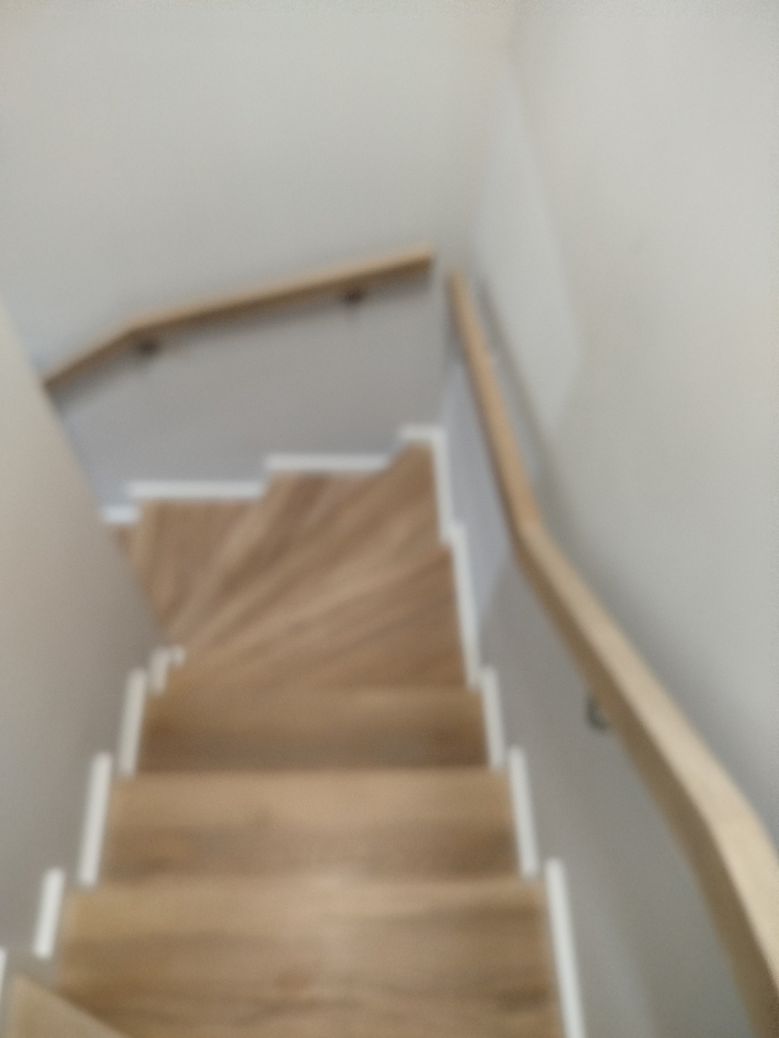 Jasne, drewniane stopnie z białymi podstopnicami i drewnianą poręczą, widziane z góry. Minimalistyczny design, neutralna kolorystyka, delikatne oświetlenie.