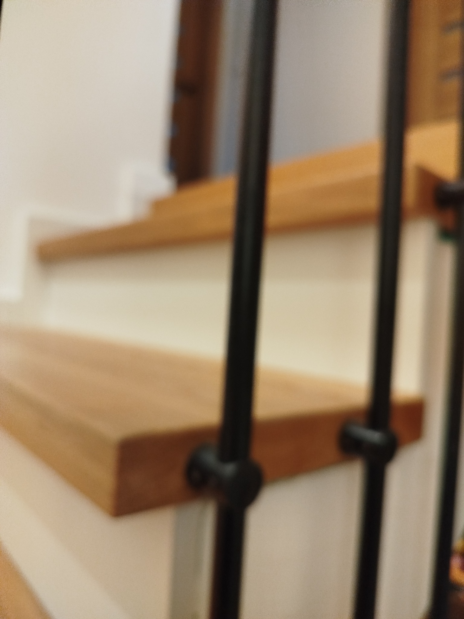 Fragment drewnianych schodów z czarną, metalową balustradą. Widoczne stopnie i elementy konstrukcyjne. Ujęcie z dołu, bliskie, z rozmytym tłem.
