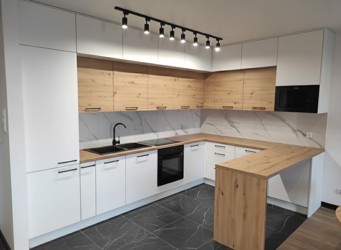Nowoczesna kuchnia w kształcie litery U z białymi szafkami dolnymi i drewnopodobnymi górnymi, czarnym blatem i marmurowym backsplashiem, oświetlona reflektorami.