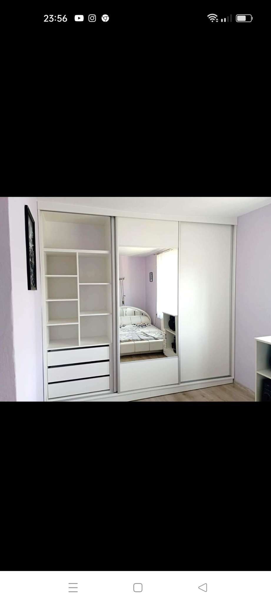 Biała szafa wnękowa z przesuwnymi drzwiami lustrzanymi, widok na wnętrze sypialni. Minimalistyczny design, jasne kolory, drewniana podłoga. Szafa z półkami i szufladami.