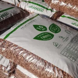Stos worków z pelletem drzewnym, zapakowanych w przezroczystą folię, z widocznym logo producenta i informacją o ekologicznym pochodzeniu.
