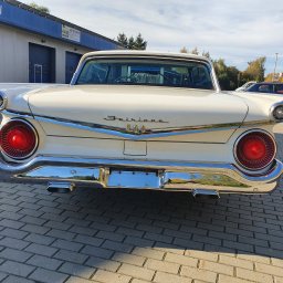 Mobilna Myjnia Parowa Steam Power Łukasz Salwin - Tył klasycznego, kremowego Forda Fairlane 500 z chromowanymi detalami, widoczny na tle budynku warsztatu samochodowego z niebieskim dachem i brukowanym podjazdem.