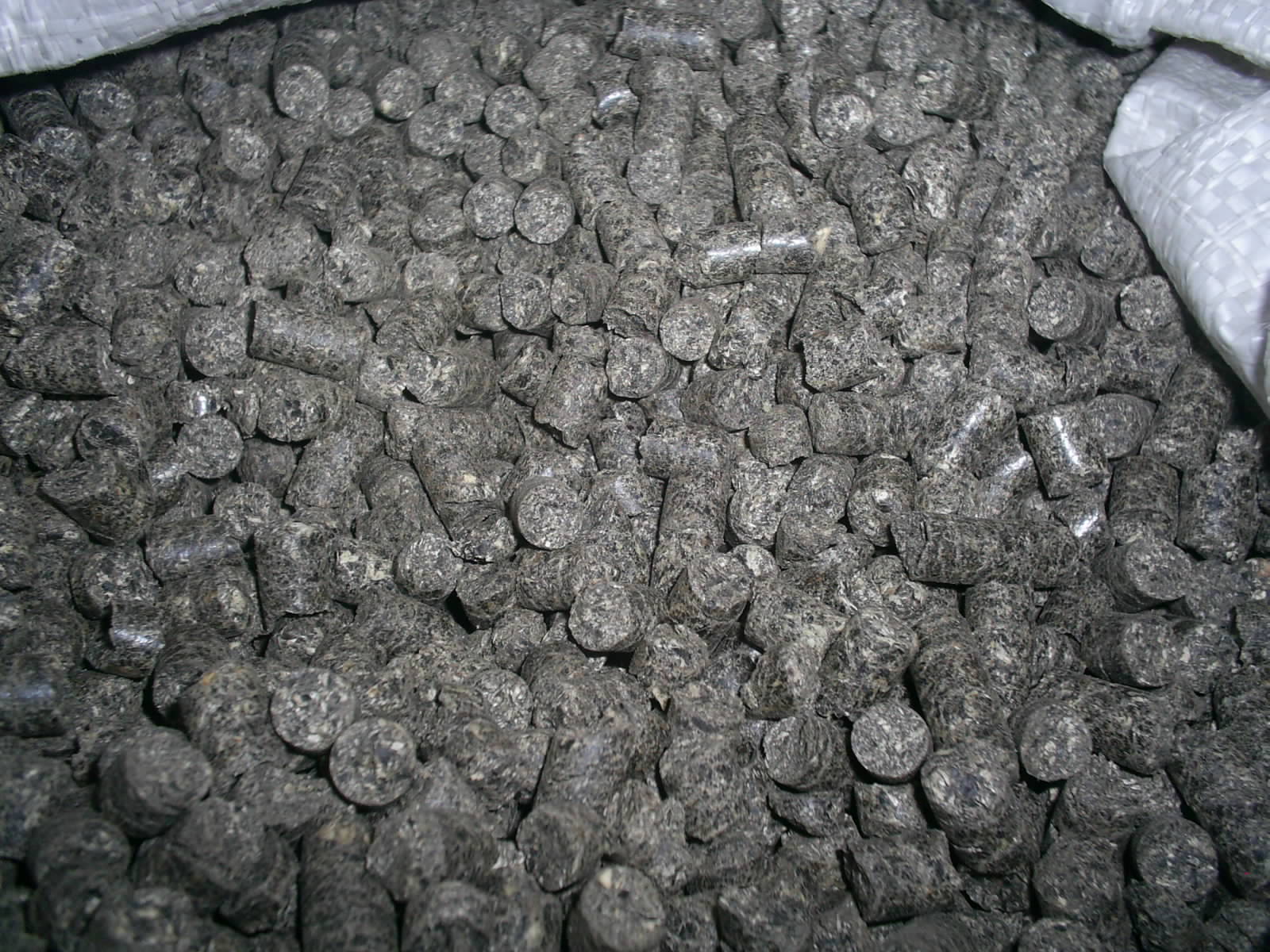 Szare pellety drzewne w worku, widoczne nierówności i struktura materiału, zbliżenie na granulki.