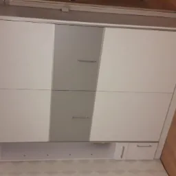 Biało-szara szafa wnękowa z przesuwnymi drzwiami, dolne szafki z szufladami, widok z dołu, jasne wnętrze.