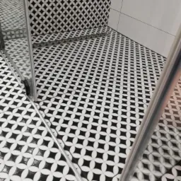 Ukończona łazienka z czarno-białą mozaiką na podłodze i ścianie kabiny prysznicowej, widoczny odpływ liniowy i fragment szklanej kabiny.