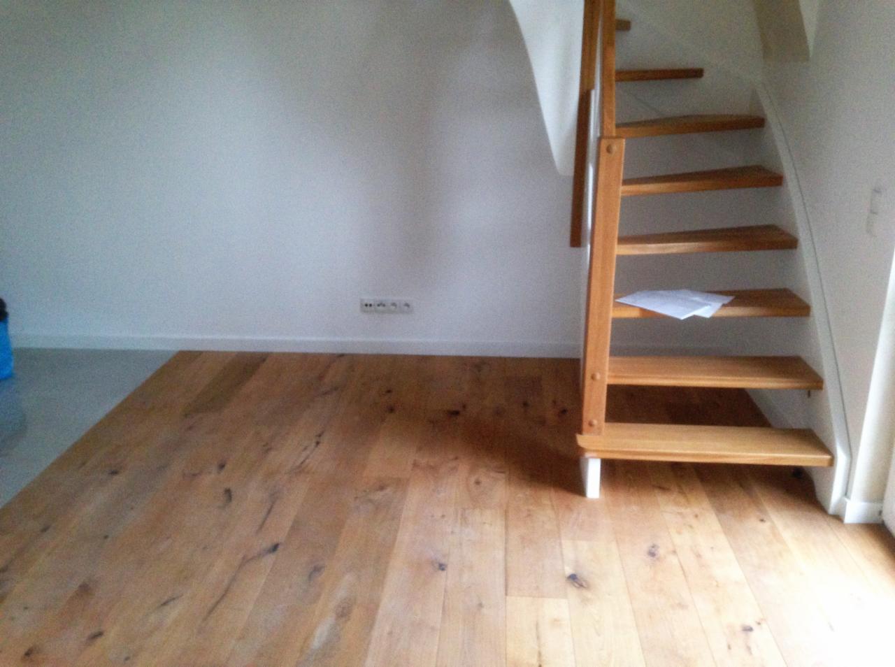 Jasna drewniana podłoga ułożona w pokoju z białymi ścianami i schodami z jasnego drewna, na jednym ze stopni leży biała kartka.