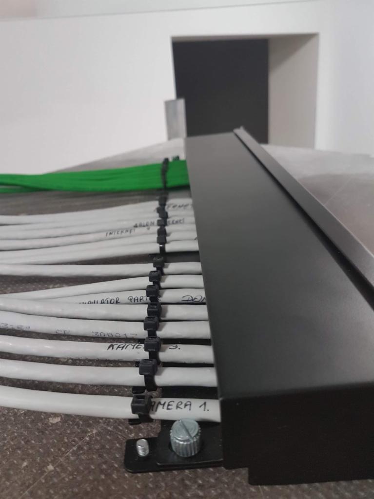 Uporządkowane kable w listwie, opisane ręcznie markerem, zabezpieczone opaskami zaciskowymi, prowadzone wzdłuż ściany.