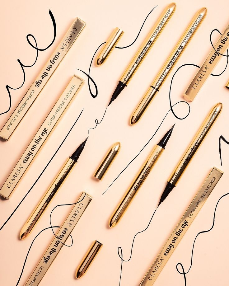 Fotografia produktowa: złote eyelinery Claresa 'Easy on the eye' na różowym tle, z czarnymi liniami imitującymi makijaż. Widoczne opakowania i otwarte produkty.