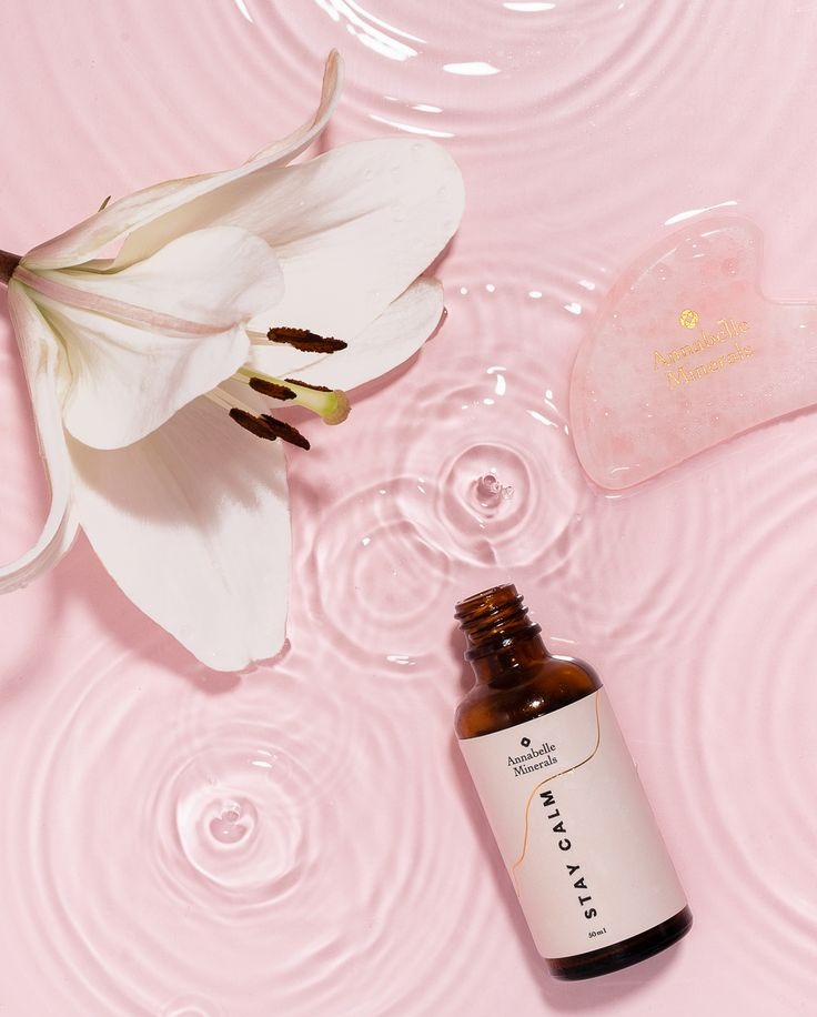 Stylizowana fotografia produktowa: olejek, gua sha i lilia na różowym tle z efektem wody. Elegancki packshot kosmetyków Annabelle Minerals do e-commerce.