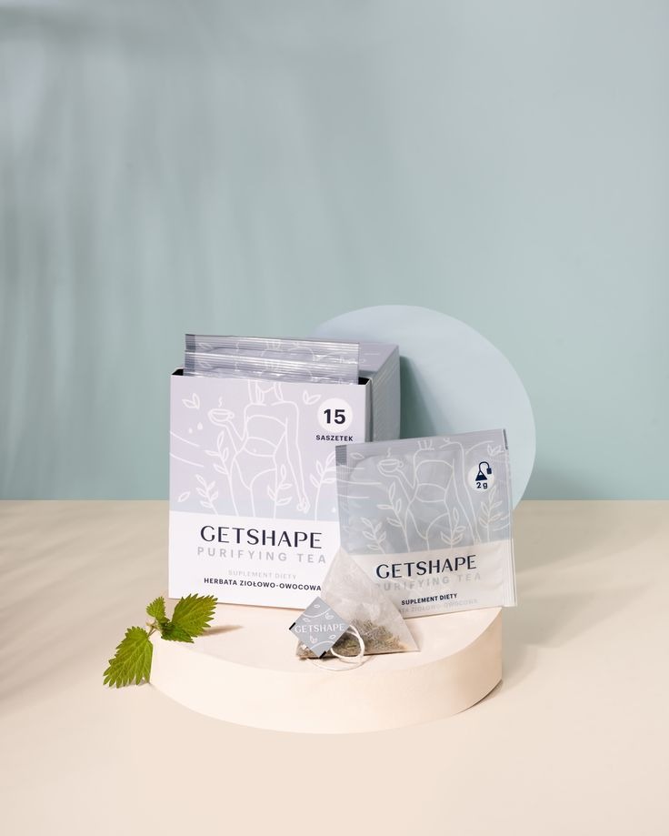 Zdjęcie produktowe herbaty ziołowej GetShape na postumencie z listkiem pokrzywy, na tle błękitnej ściany i jasnego koła. Minimalistyczna kompozycja, delikatne cienie.