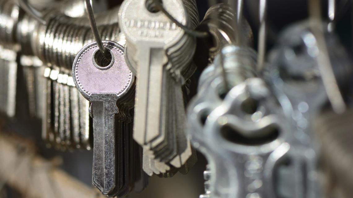 Pęk kluczy na metalowych kółkach, z bliska widoczne detale wykończenia główek i ząbków, w tle rozmyte kontury kolejnych kluczy.