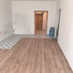 fliesen-tech - Wnętrze w trakcie prac: ułożone płytki podłogowe z wzorem i panele imitujące drewno. Ściany przygotowane do malowania, widoczny worek z odpadami budowlanymi.