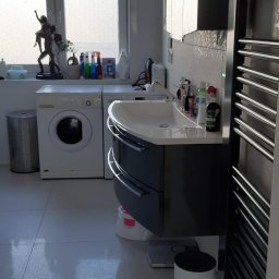 fliesen-tech - Nowoczesna łazienka z umywalką w zabudowie, pralką pod oknem i grzejnikiem drabinkowym. Jasne płytki podłogowe i dekoracje.