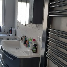 fliesen-tech - Nowoczesna łazienka z umywalką na szafce w kolorze grafitowym, lustrem w szafce i grzejnikiem drabinkowym. Na blacie kosmetyki i akcesoria łazienkowe.