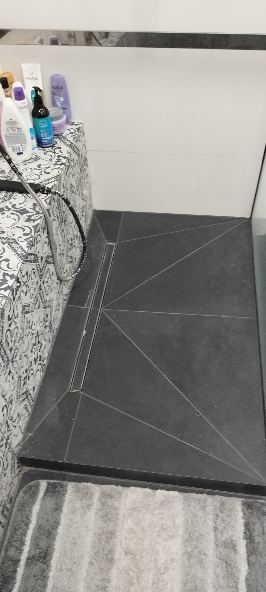 Nowoczesna łazienka z ciemnymi płytkami podłogowymi ułożonymi w geometryczny wzór, liniowy odpływ prysznicowy i dekoracyjne płytki ścienne.