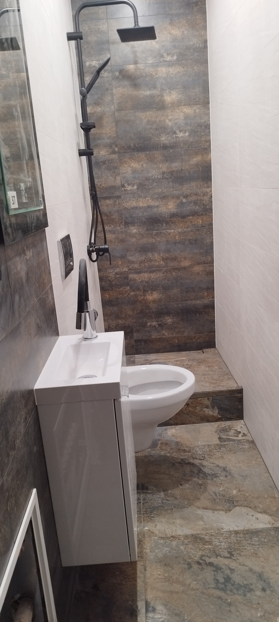 Stylowa, wykończona łazienka w Strzegomiu z szaro-brązowymi płytkami, białą umywalką z szafką i czarną armaturą, ukazana w całościowym ujęciu.