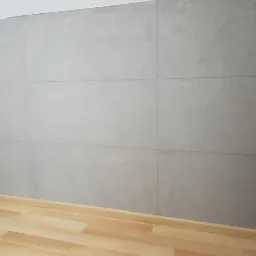 Ściana pokryta szarymi płytami imitującymi beton, z widocznymi fugami i fragmentem drewnopodobnej podłogi.