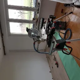 Ukośnica Metabo na statywie, odkurzacz przemysłowy i fragment ułożonej podłogi z paneli w pokoju z widokiem na zewnątrz przez okno.