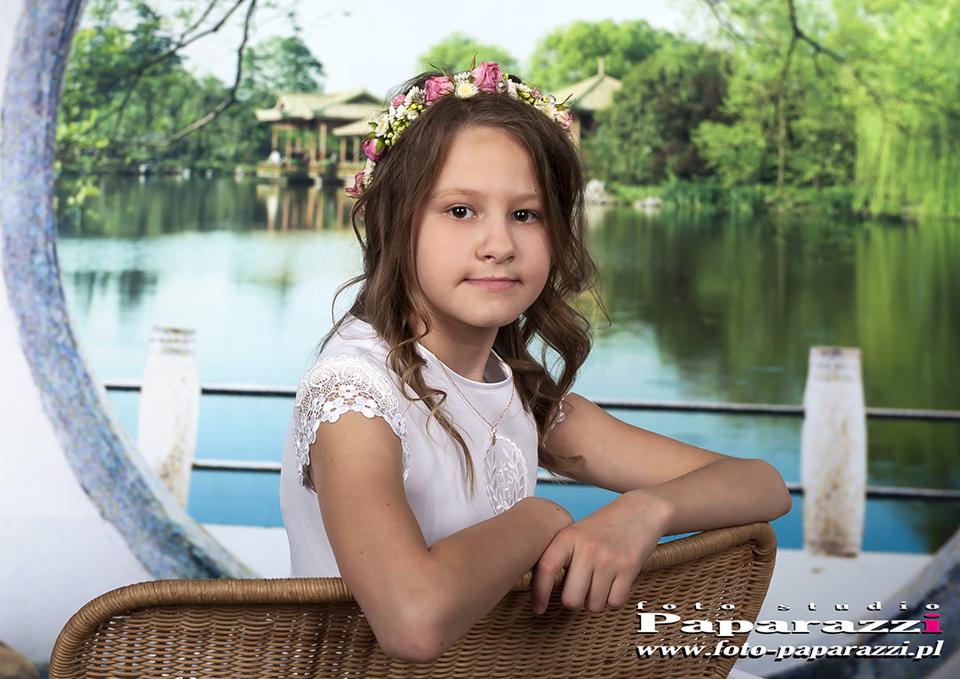 Portret dziewczynki w białej sukience z wiankiem na głowie, siedzącej na wiklinowym krześle na tle jeziora i azjatyckiej architektury, wykonany w studio.