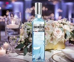 Butelka wódki Amundsen na stole z dekoracjami kwiatowymi i świecami, ustawiona na tle rozmytego wnętrza sali bankietowej.