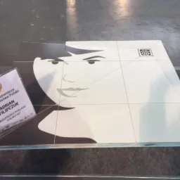 Ułożona z płytek mozaika przedstawiająca twarz kobiety, obok wizyt&oacute;wka 'VII Glazurnicze Mistrzostwa Polski', widoczny odpływ liniowy