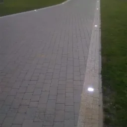 Oświetlony podjazd z kostki brukowej z wbudowanymi lampkami LED wzdłuż krawędzi i trawnika.