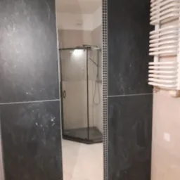 Wykończona łazienka z czarnymi płytkami imitującymi marmur, kabina prysznicowa w tle, biały grzejnik drabinkowy po prawej stronie.