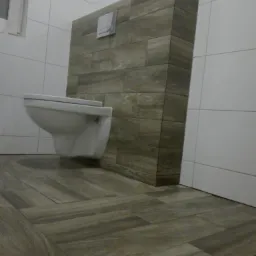 Nowoczesna toaleta wisząca z zabudową z płytek imitujących drewno, dopasowanych do podłogi, białe płytki na ścianach, minimalistyczny design.