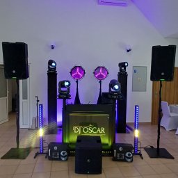 Oskar Wawrzynowicz - Profesjonalny sprzęt DJ-ski z podświetlanym panelem 'DJ Oscar', kolumny, reflektory i oświetlenie LED w przestronnym wnętrzu, gotowy do występu.