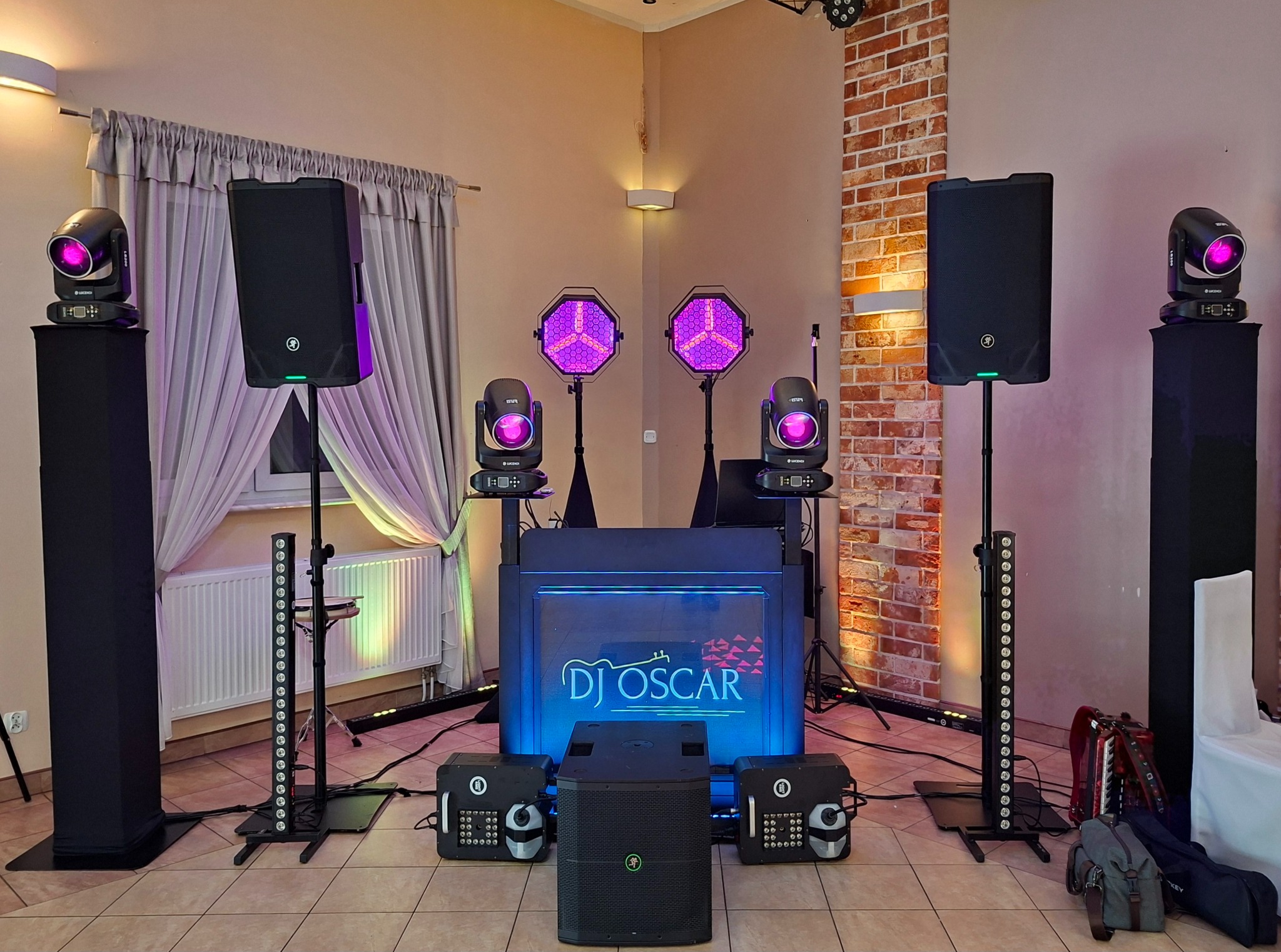Kompletny zestaw DJ'ski z oświetleniem scenicznym i nagłośnieniem, gotowy do występu. Widoczne kolumny, reflektory LED i konsoleta z podświetlanym logo 'DJ Oscar'.