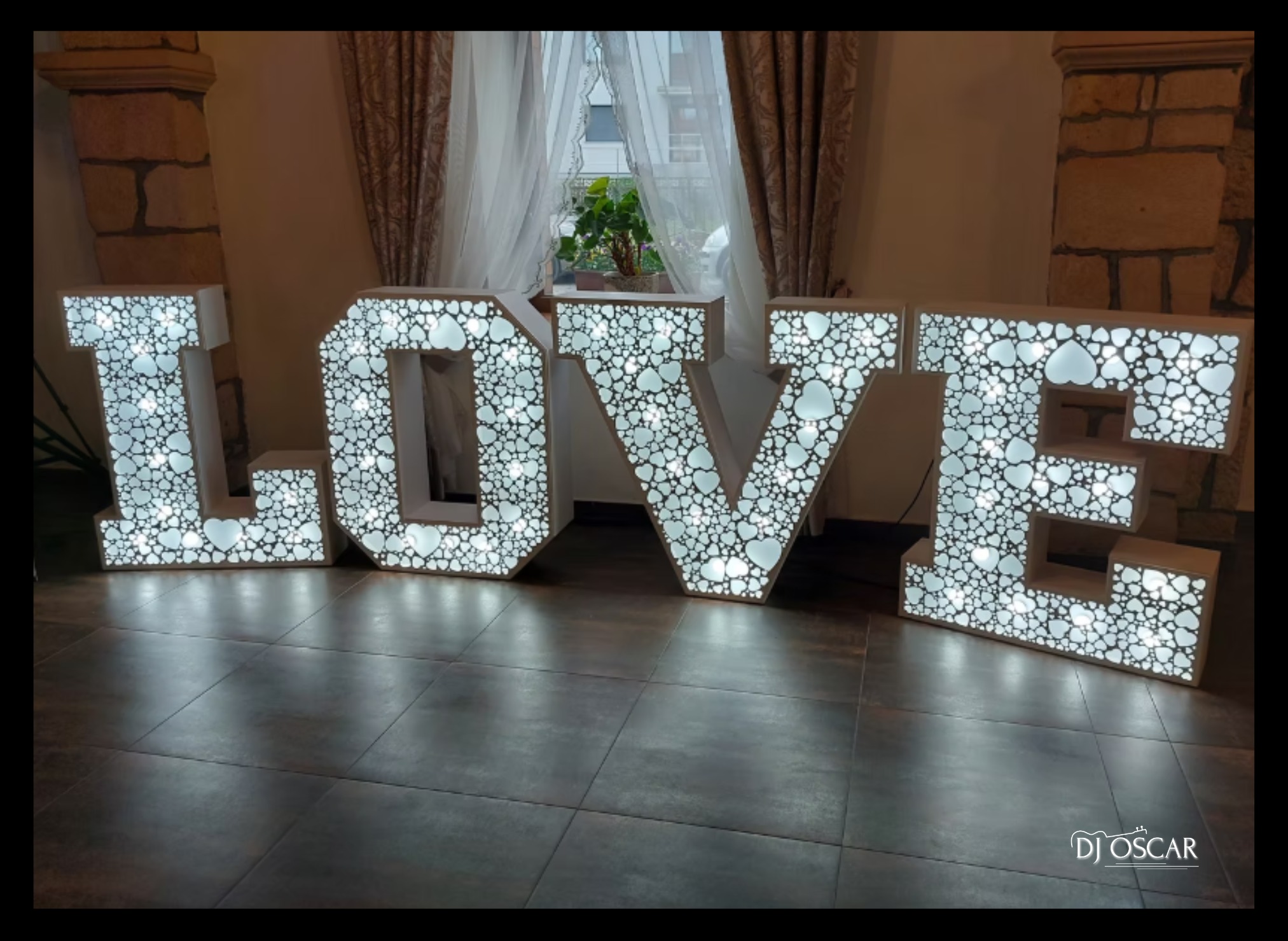 Świecący napis LOVE z serduszkami, dekoracja sali weselnej. Duże, białe litery podświetlone diodami LED, ustawione na podłodze z płytek. Romantyczny klimat.