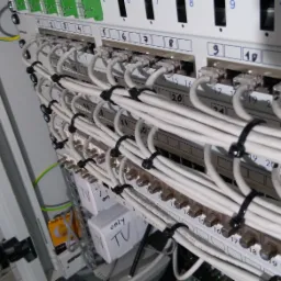 Panel krosowniczy z podłączonymi kablami sieciowymi i koncentrycznymi, oznaczony złączkami TV, widoczne przewody uziemiające