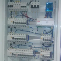 Wewnętrzny widok rozdzielnicy elektrycznej z zainstalowanymi bezpiecznikami, modułami i okablowaniem, widoczne elementy marki Eaton.