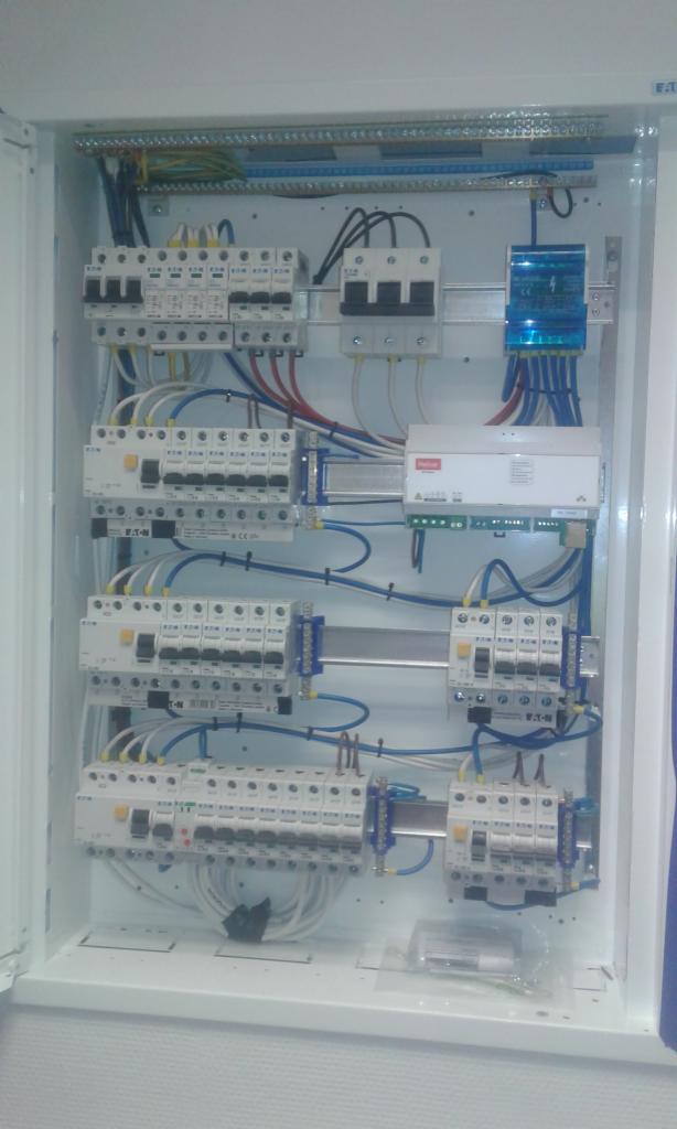 Wewnętrzny widok rozdzielnicy elektrycznej z zainstalowanymi bezpiecznikami, modułami i okablowaniem, widoczne elementy marki Eaton.