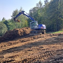 Bojarczuk Mariusz -Koparki - Niebieska koparka Atlas 105 M nabiera ziemię na nierównym terenie w słoneczny dzień, w tle drzewa i częściowo widoczny biały samochód.