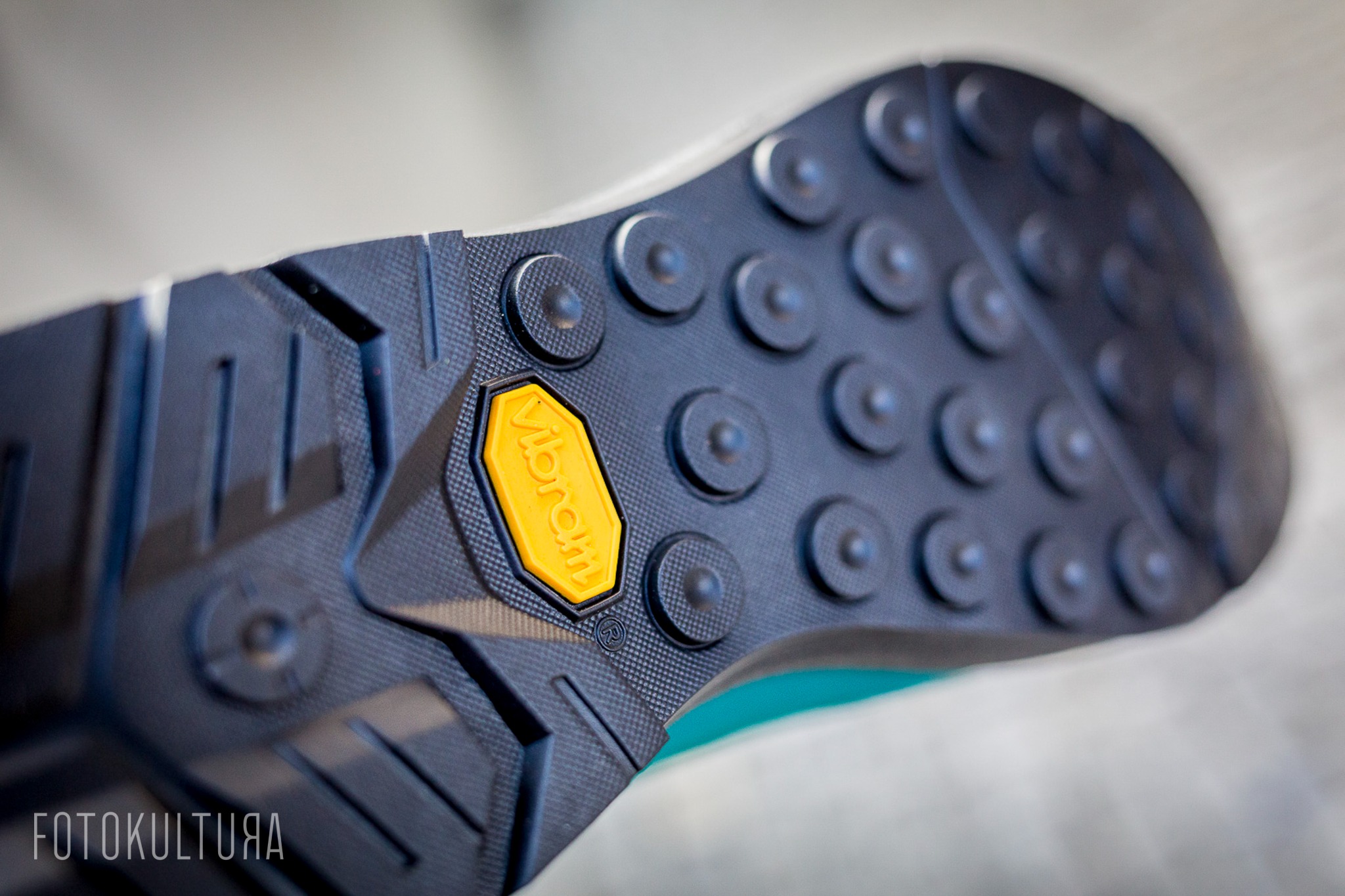 Szczegółowe zbliżenie podeszwy buta trekkingowego z wyraźnie widocznym żółtym logo Vibram i okrągłymi wypustkami antypoślizgowymi na ciemnej, teksturowanej gumie.