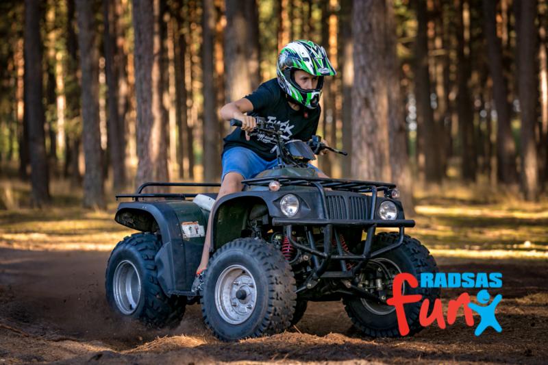 Chłopiec w kasku jeździ na quadzie po leśnej ścieżce, widoczne drzewa w tle i logo 'RADSAS Fun' w prawym dolnym rogu.