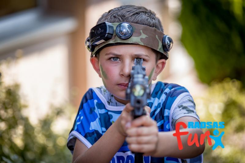 Chłopiec z zielonymi plamkami na twarzy, w kamuflażowej koszulce, celuje z pistoletu laserowego, nosząc na głowie specjalną opaskę z czujnikami.