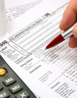 Wypełnianie formularza podatkowego 1040 z użyciem kalkulatora i czerwonego długopisu, zbliżenie na dłoń i dokument.