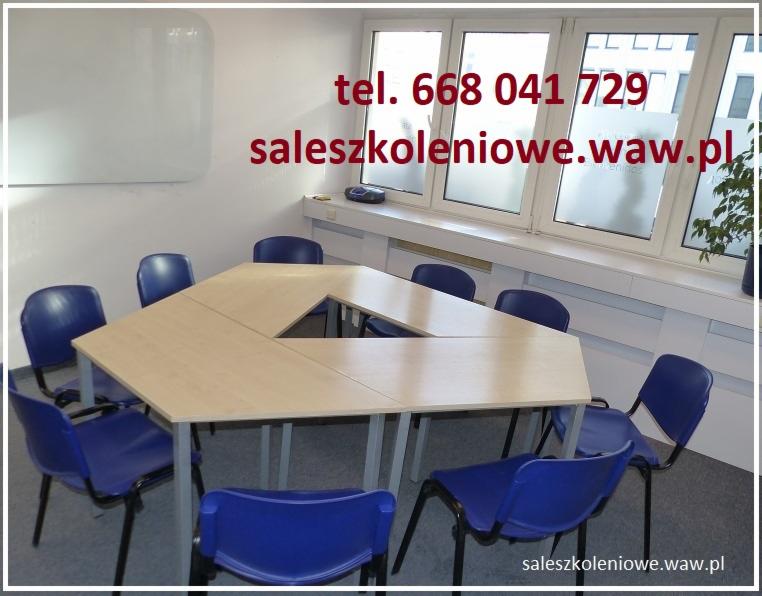 Sala szkoleniowa z trapezoidalnym stołem i krzesłami, tablica suchościeralna na ścianie, okno z częściowo zamazaną szybą, widoczny numer telefonu i adres strony internetowej.