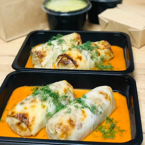 Gotowe gołąbki w czarnych pojemnikach z sosem pomidorowym i koperkiem, zapakowane na wynos, widok z góry.