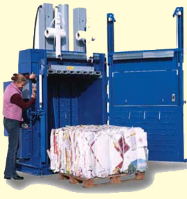 Niebieska belownica hydrauliczna w trakcie pracy, operator obsługuje maszynę, sprasowane materiały na palecie wewnątrz komory.