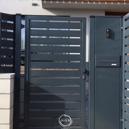 Furtka palisadowa z profili 10x2, prześwit 2,5 cm ze słupkiem multimedialnym w kolorze grafit RAL7016. Wmontowana skrzynka na listy oraz domofon.