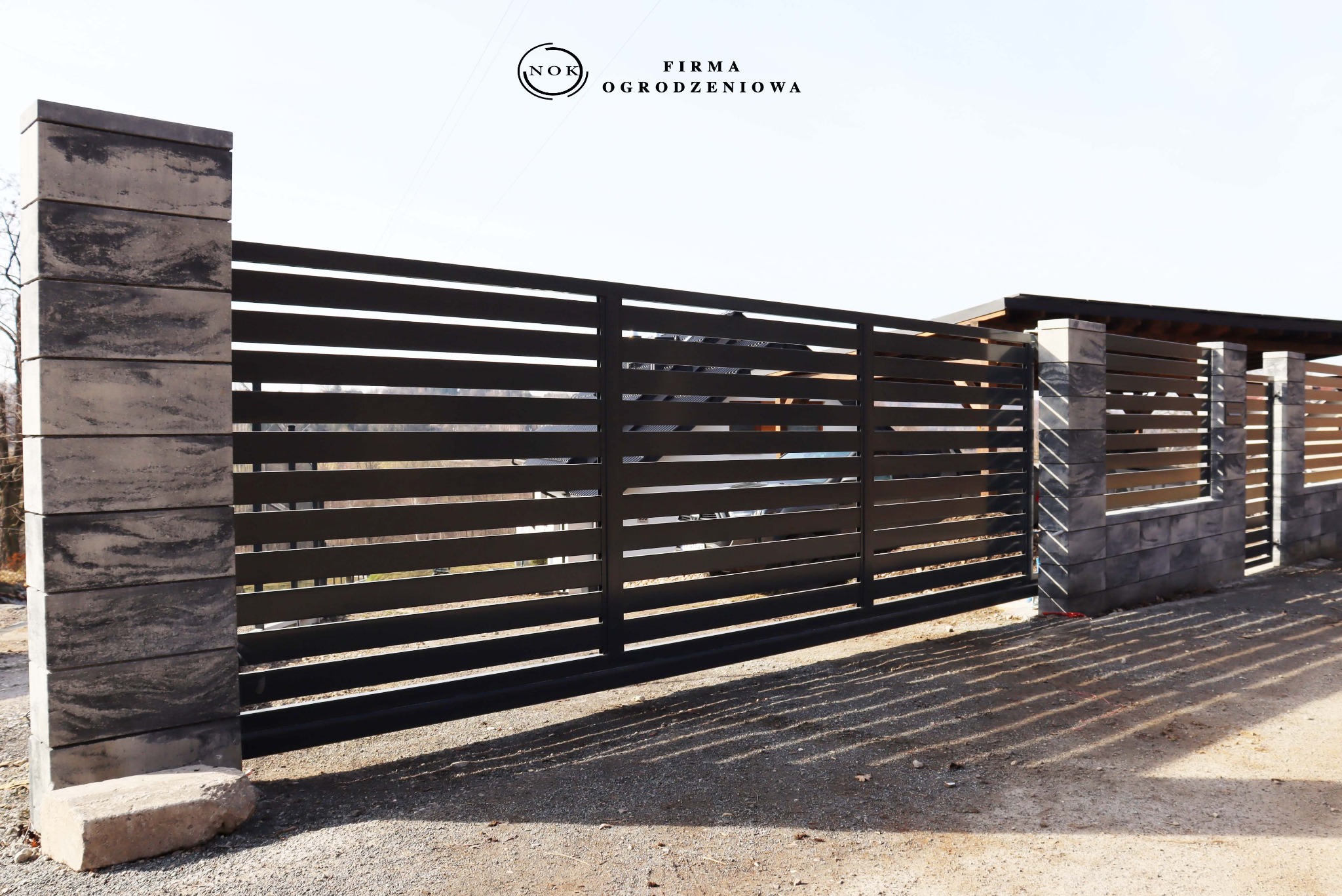 Nowoczesna brama przesuwna palisadowa z czarnymi profilami, zamontowana do bloczków Joniec Roma Horizon Onyx. Minimalistyczny design.